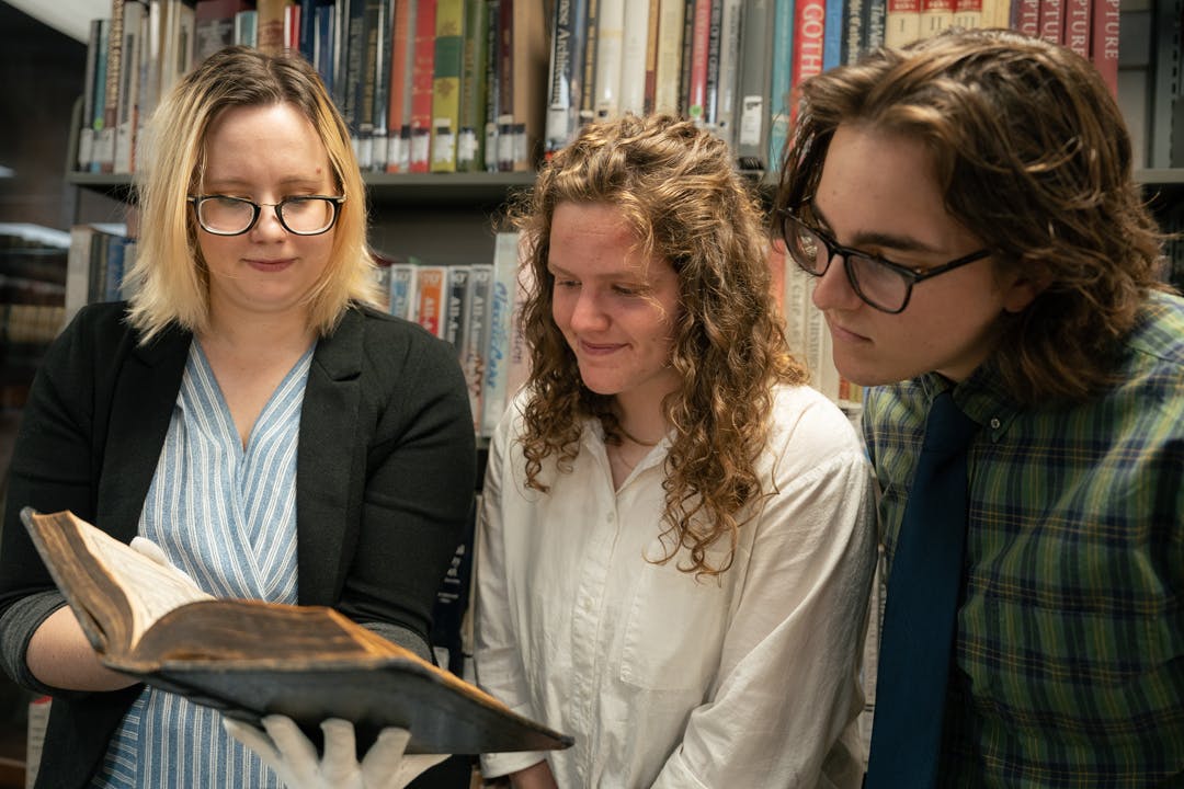 Librarian Rebekah Leidenfrost with students examining an old book at Tyndale Library